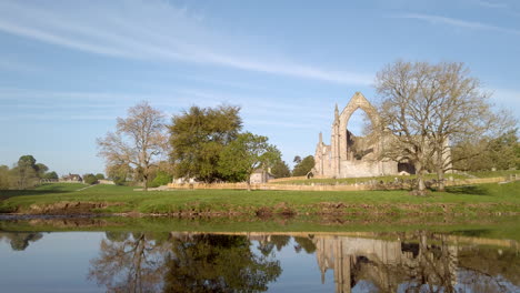 Toma-Panorámica-De-Las-Ruinas-De-La-Abadía-De-Bolton-En-Una-Hermosa-Mañana-De-Verano-En-Yorkshire,-Inglaterra,-Revelando-El-Cruce-Del-Río