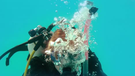 mujer con equipo de buceo mirando la cámara bajo el agua