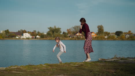 pleased mother and preschooler girl walk on bank of river
