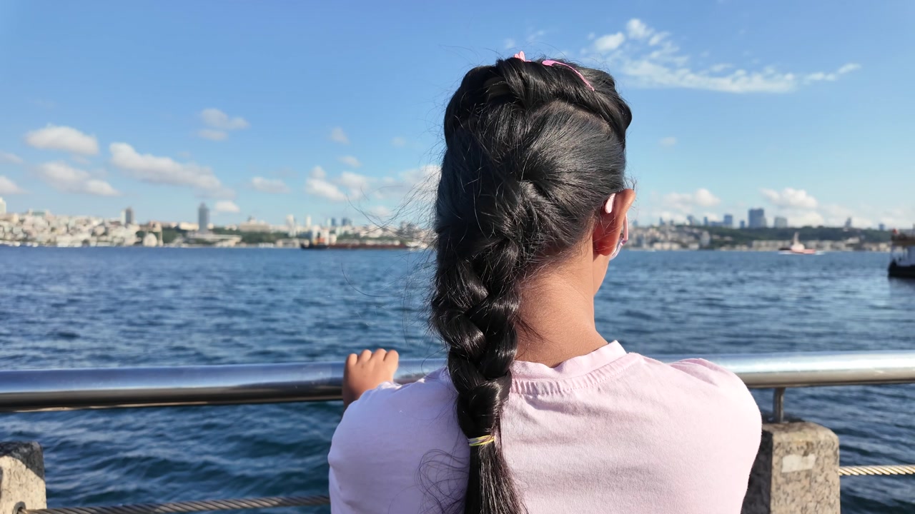 Young Girl with Braided Hair Looking at City Skyline Across the Sea
