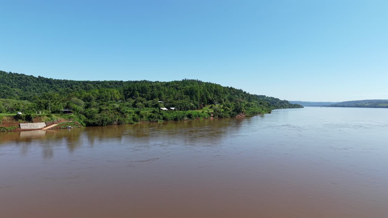 A stunning, low-altitude aerial flight over a wide, brown river in the Misiones province of Argentina. The drone captures the lush, green subtropical forests lining the riverbanks