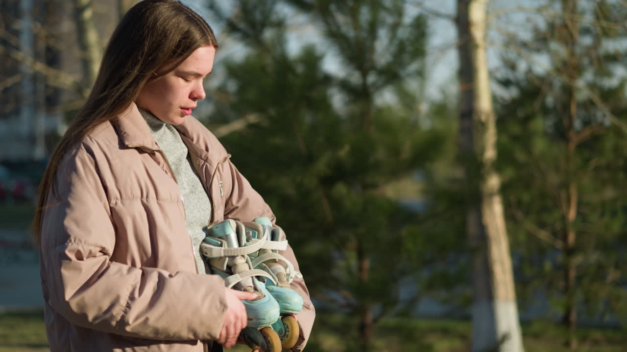 공원을 걸으면서 스케이트보드를 들고 다니는 소녀의 측면. 그녀는 은 날 야외 환경을 즐기면서 평온한 표정으로 복아 재과 회색 내부 셔츠를 입고 있습니다.