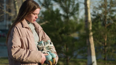 side shot of a girl carrying a skateboard while walking through a park. she is wearing a peach jacket and a grey inner shirt, with a calm expression as she enjoys the outdoor environment on sunny day