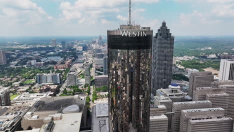 aerial ascending footage of modern cylindrical high rise building with glossy glass facade reflecting surround