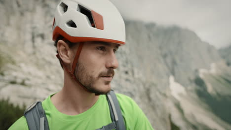 A-young-hiker-looking-at-the-view,-wearing-a-white-colored-helmet-with-orange-stripes