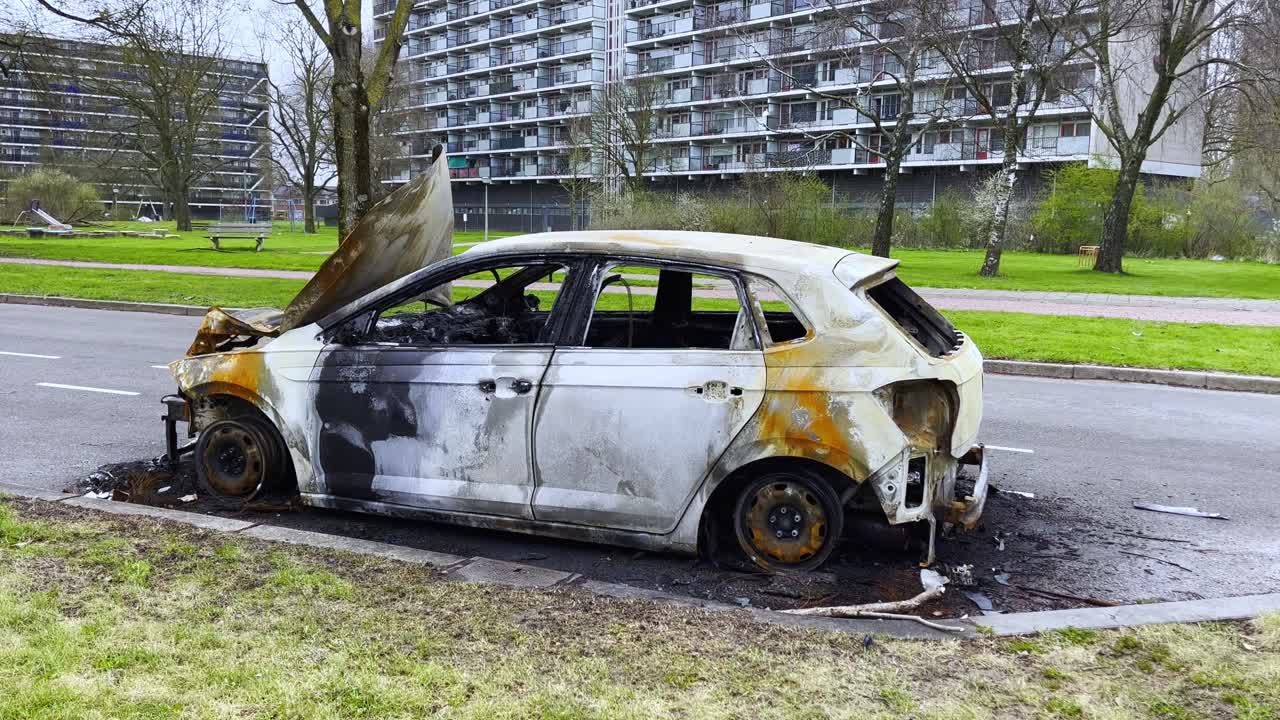 Nærbillede af et forkullet hvidt bilskrog efterladt i vejkanten i Arnhem, med smeltet interiør og udblæste vinduer efter en intens brand.