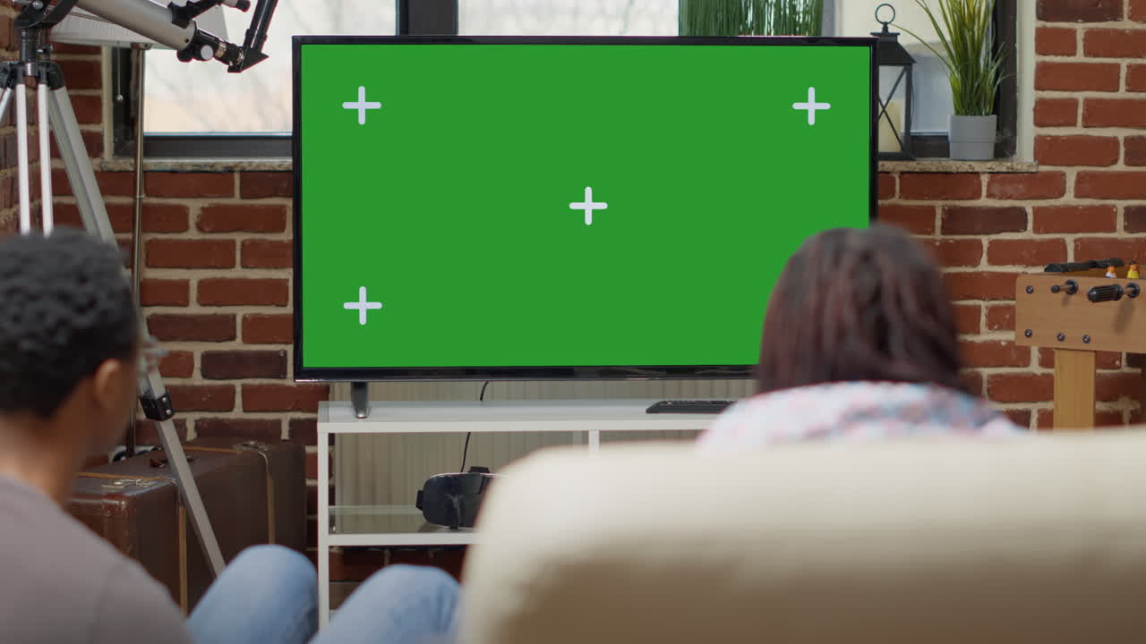 Men and women watching television display with green screen