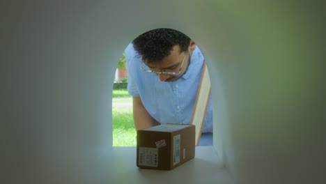 postal worker putting parcel and envelopes in mailbox