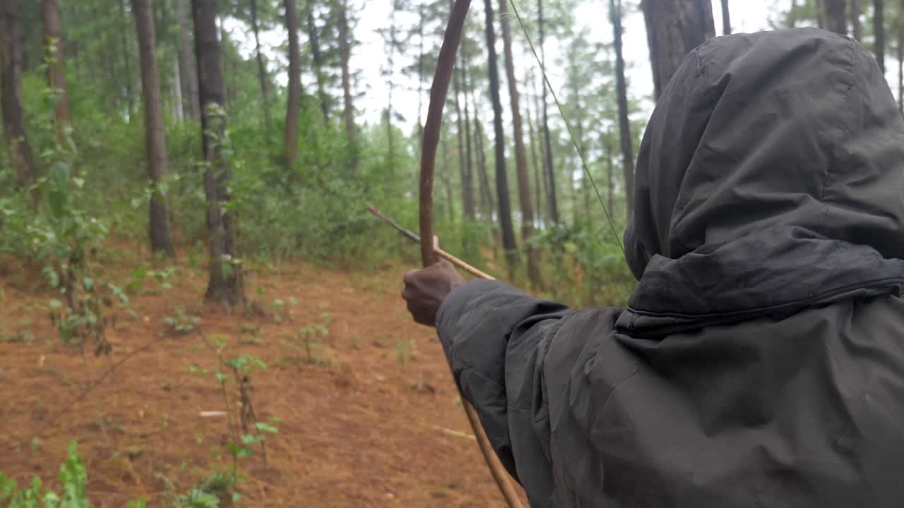 전통적인 활과 화살로 조준하고 아프리카의 숲에서 쏘는 아프리카 사냥꾼 어깨 뒤에서 클로즈업 샷