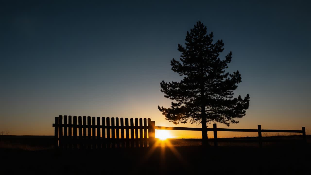 Silhouetted Tree and Fence Against a Vibrant Sunset Sky: A Tranquil Evening Scene of Nature's Beauty and Peacefulness Captured in Stunning Detail