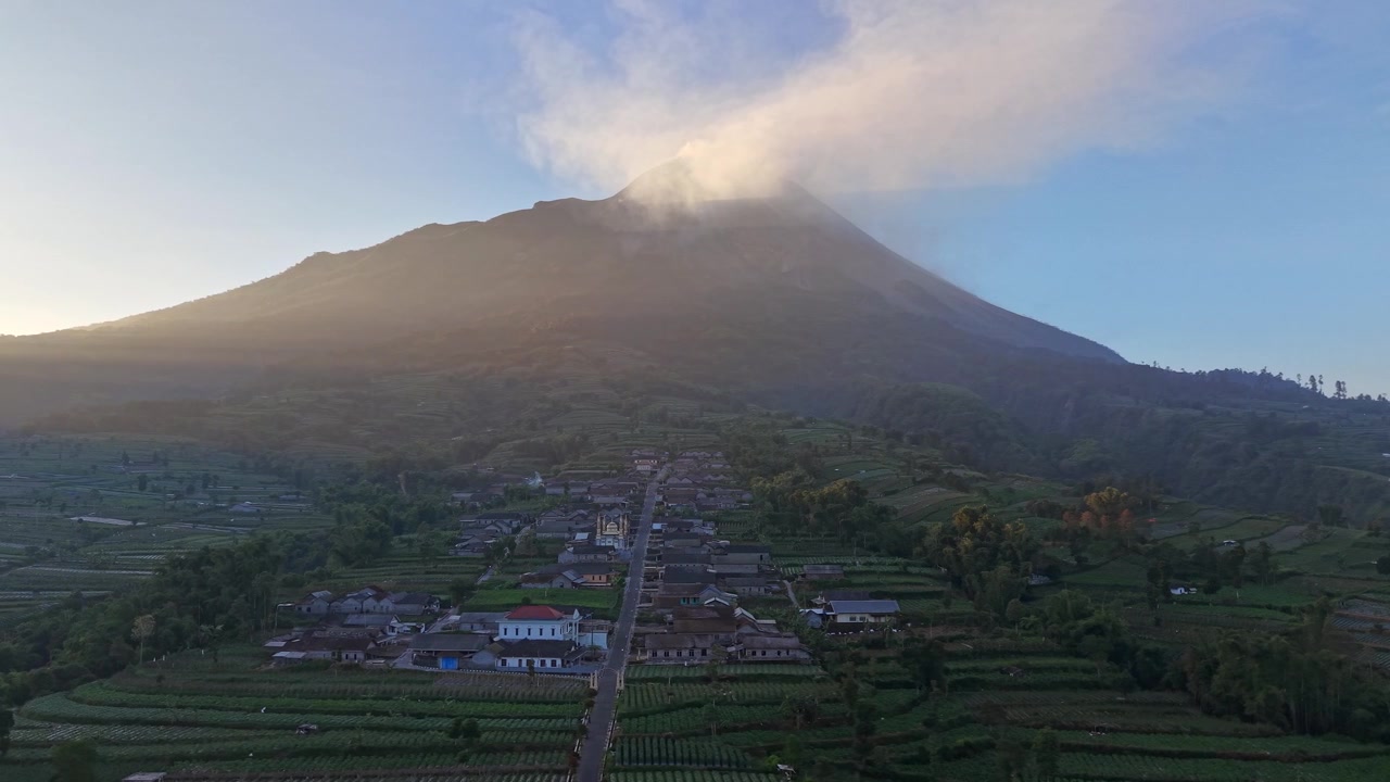 La luce dell'alba illumina il Monte Merapi e la campagna circostante. Case rurali, campi verdi e terreno vulcanico creano una vista affascinante