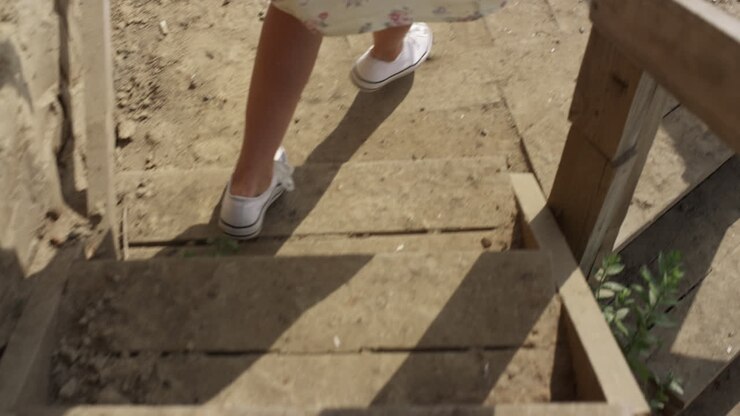 Donna che scende le scale di legno verso la spiaggia, primo piano. Gambe snelle di ragazza con le scarpe da ginnastica.