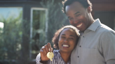 Portrait-Of-Hugging-Couple-Standing-Outdoors-In-Front-Of-House-Holding-Keys