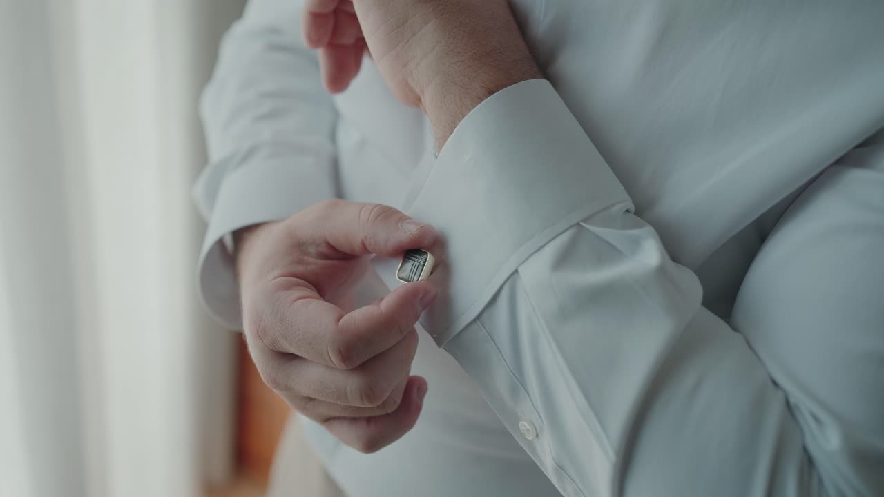 Close view of man hand securing cufflink on white dress shirt sleeve while dressing for formal occasion indoors