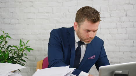 a stressed businessman using a calculator to add up bills and taxes with piles of paperwork