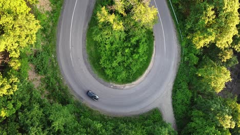 Luftaufnahme-Eines-Autos,-Das-Im-Sommer-Auf-Einer-Kurvigen-Straße-An-Einem-Wald-Vorbeifährt