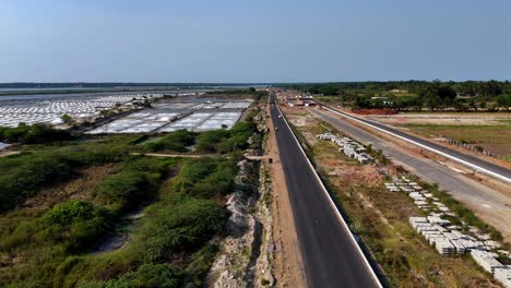 Drone footage captures a new highway&#039;s progress in Chennai to pondicherry ECR, stretching past large salt pans and a gas station, showcasing the development of modern transportation infrastructure