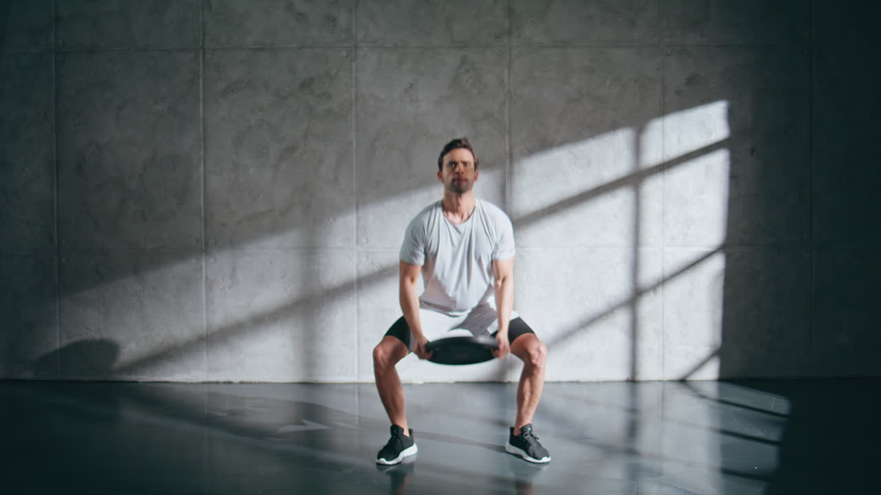 Sport trainer doing lunges using weight plate at studio. Guy workout routine