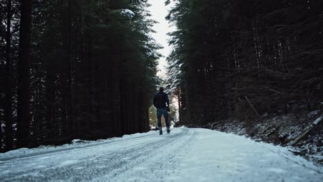 Young-man-hiking-over-a-road-in-a-dense-spruce-forest,-throwing-his-arms-up-in-the-air-of-happiness-and-excitement