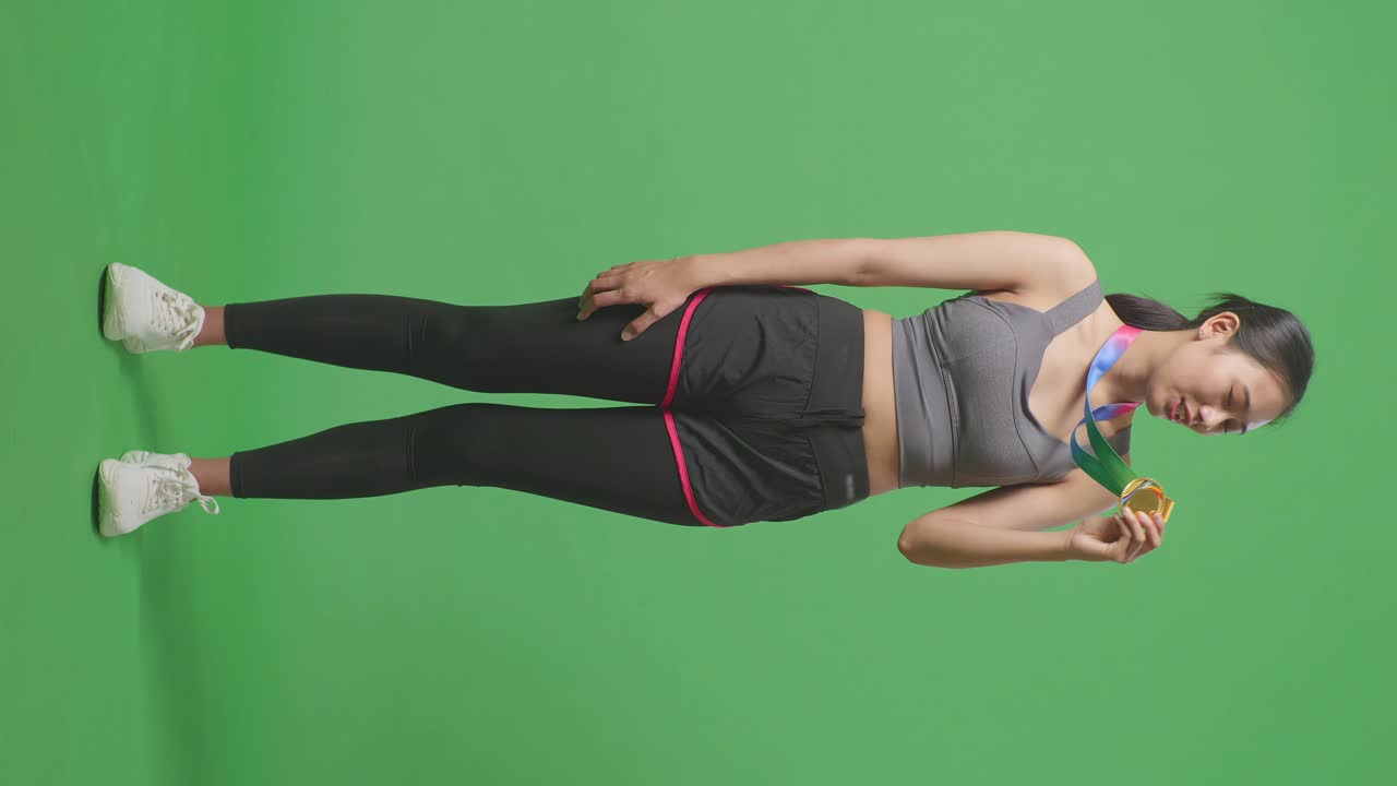 cuerpo lleno de mujer asiática besando una medalla de oro en su mano estando orgulloso de ganar como el primer ganador en el fondo de la pantalla verde en el estudio