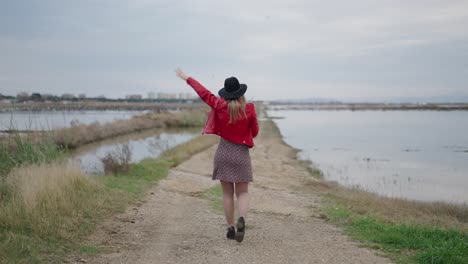 woman in red jacket walking along a country road by a lake