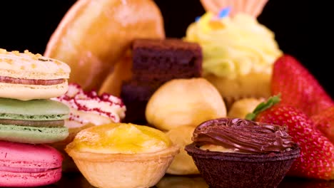 colorful macarons, brownies, cupcakes, tarts, donuts, and strawberries arranged on black background under bright lighting