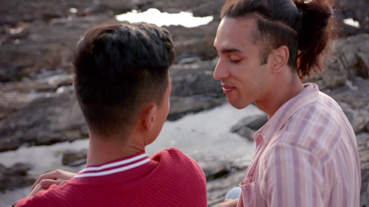 Coppia gay maschile felice e diversificata che si abbraccia in spiaggia, al rallentatore