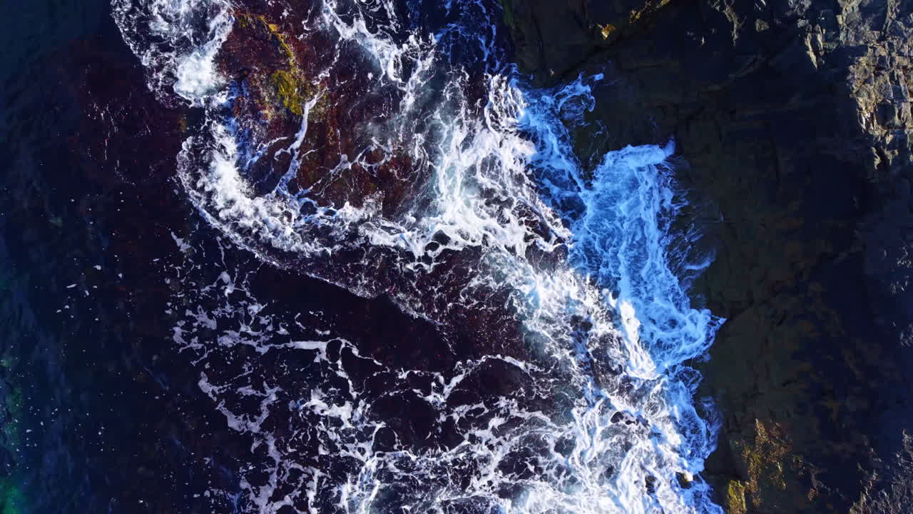 Waves crash against vibrant rocky shoreline at sunrise, creating a mesmerizing dance of color and foam that celebrates nature's beauty and power