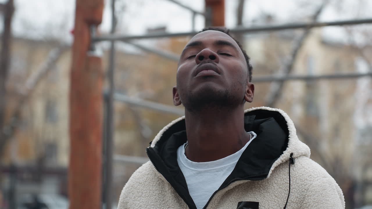 joven realizando un ejercicio de torsión profunda del cuello al aire libre en invierno, perdido en la concentración con un fondo con árboles y edificios desnudos, nieve en el suelo en un entorno urbano