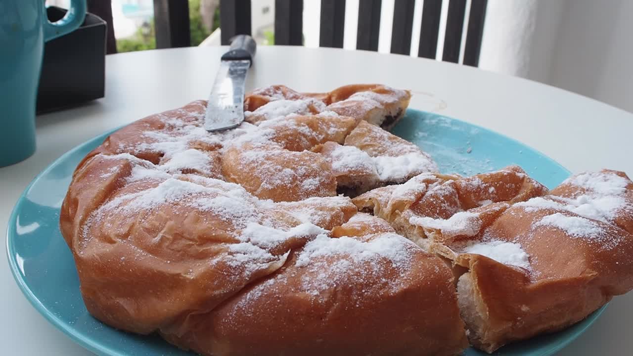 Fluffy chocolate-filled Ensaimada on a plate with powdered sugar, knife on the side
