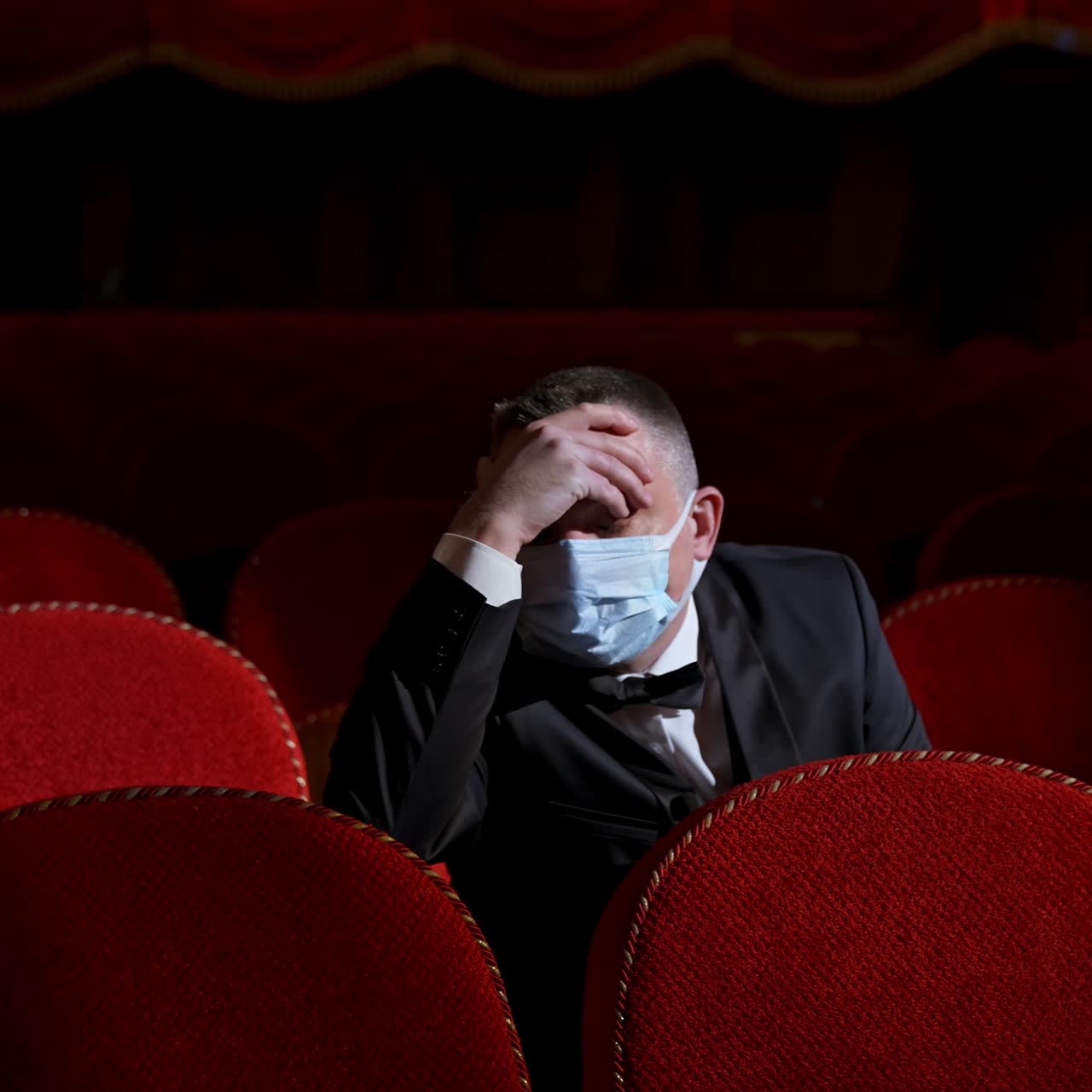 Tired businessman in medical mask in empty theater. Man with bad well-being is sitting in auditorium without people. Covid-19