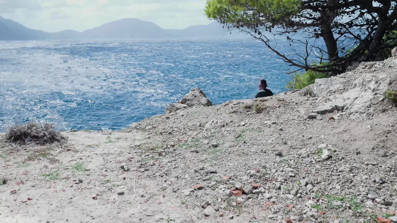 Man Sitting on Cliff overlooking the Ocean