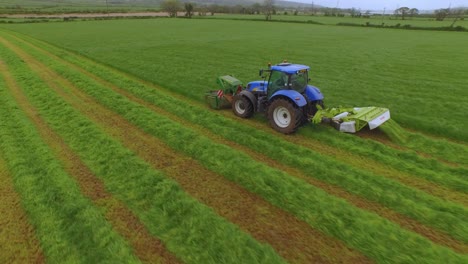 aerial view of a tractor cutting the grass in a large green field