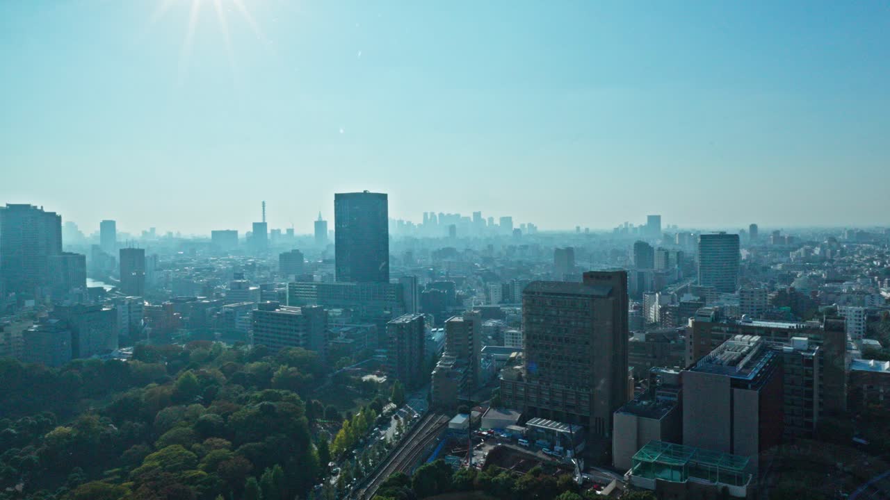 A sweeping panoramic view of Tokyo's sprawling cityscape from Bunkyo-ku, under a bright, hazy sky. Buildings and green spaces extend to the horizon.