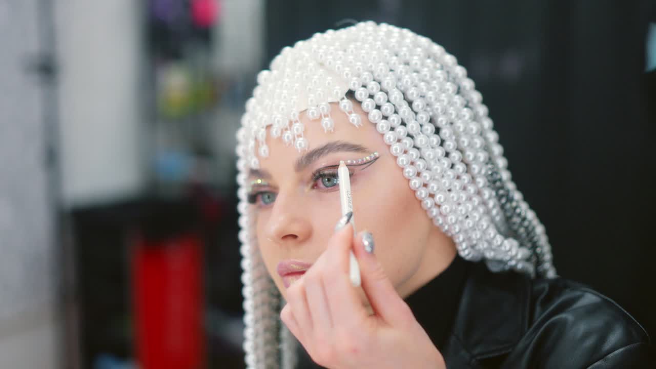 Woman applying dramatic eye makeup with a pearl headpiece