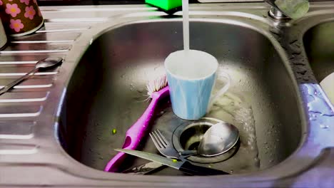 water cascades from the tap, splashing into the stainless steel sink, where plates and utensils wait patiently