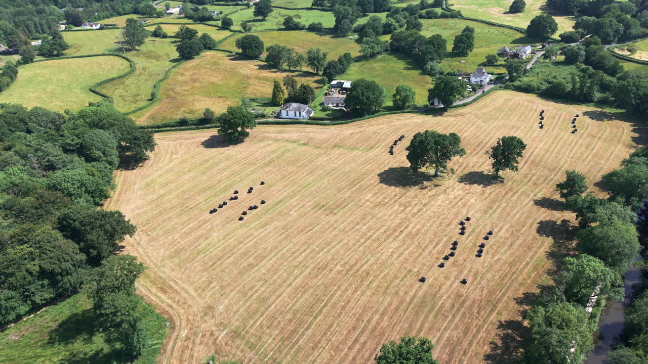 Slow orbiting drone footage of a harvested hay field with silage bales in summer