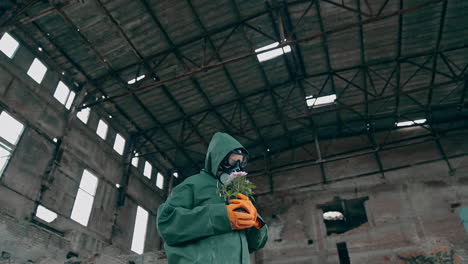 ecologist with plants in abandoned place. person in protective uniform and gas mask holding flowers inside the destroyed building. chemical attack and air pollution.