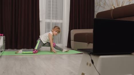 children girl watching online distance lessons with trainer on laptop, exercising twine at home