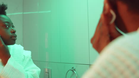 african american woman applying face toner in bathroom