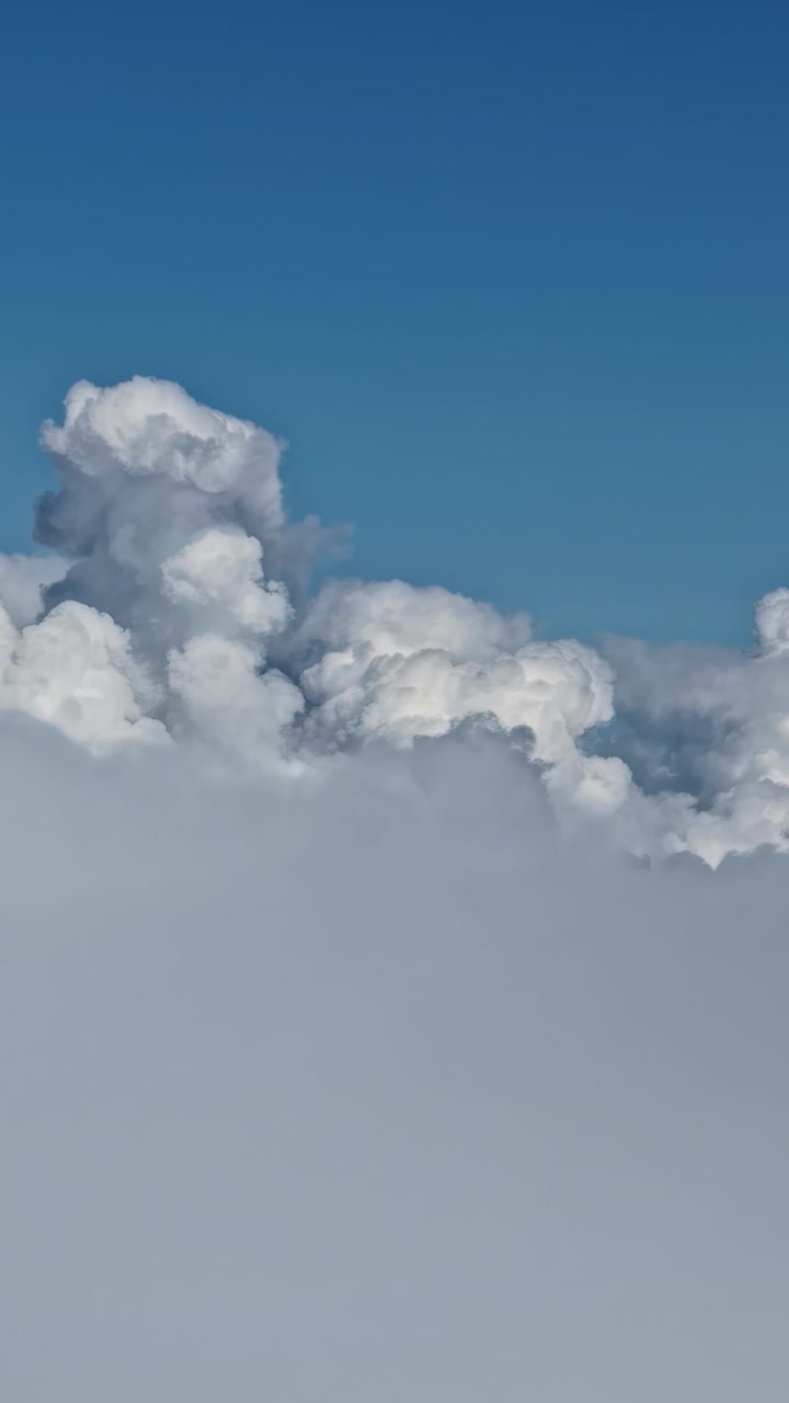 Towering white cumulus clouds rise above a dense cloud layer under blue sky