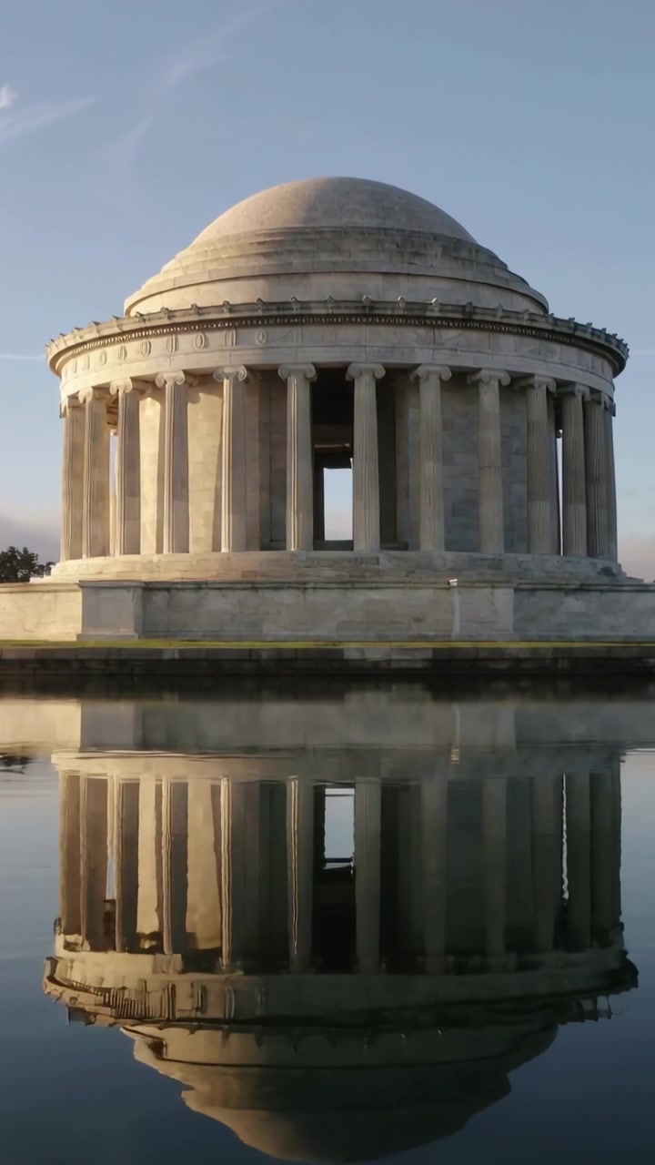 Video verticale: Luce solare mutevole che illumina una rotonda a cupola presso un monumento commemorativo, con uno specchio d'acqua che riflette la base