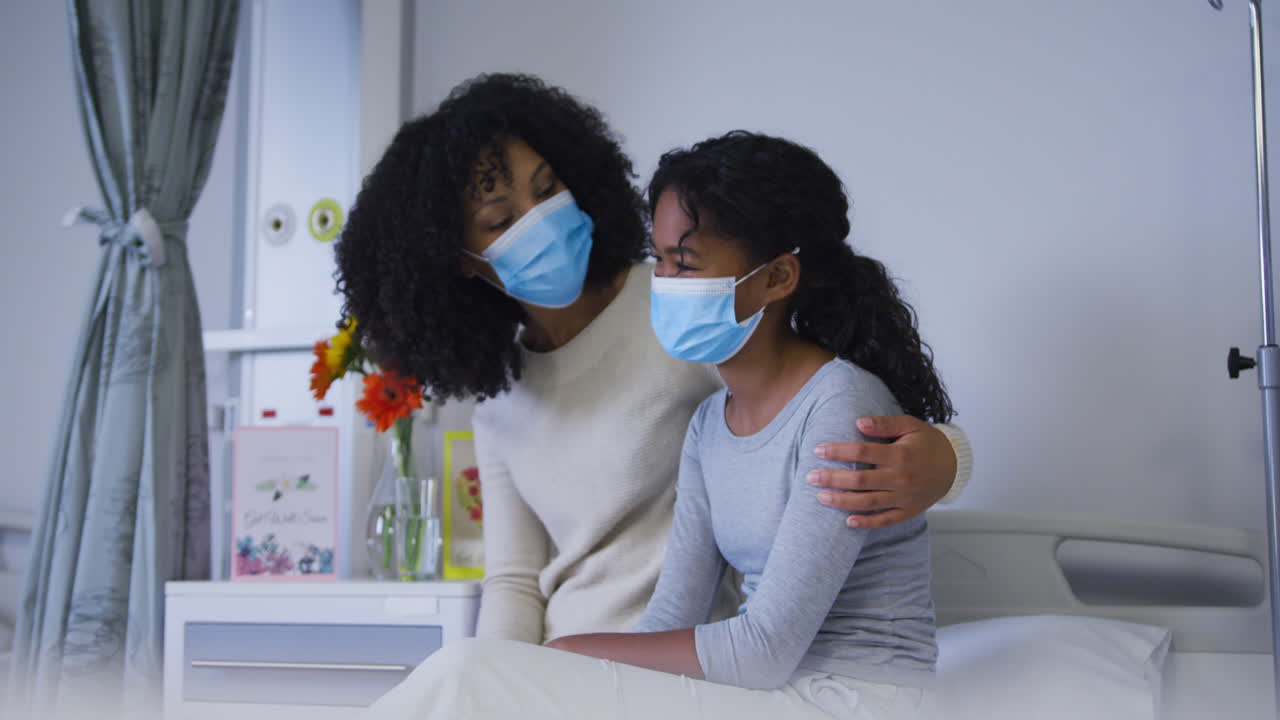 African american mother wearing face mask taking and comforting her daughter at hospital