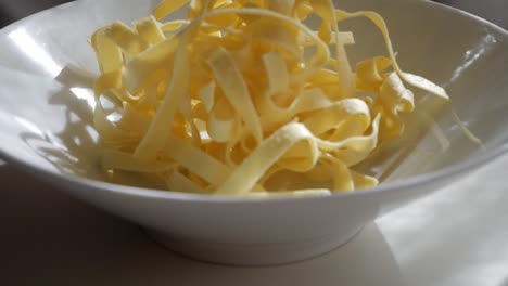 fresh pasta fettuccine in white bowl, raw noodles with warm morning sunlight