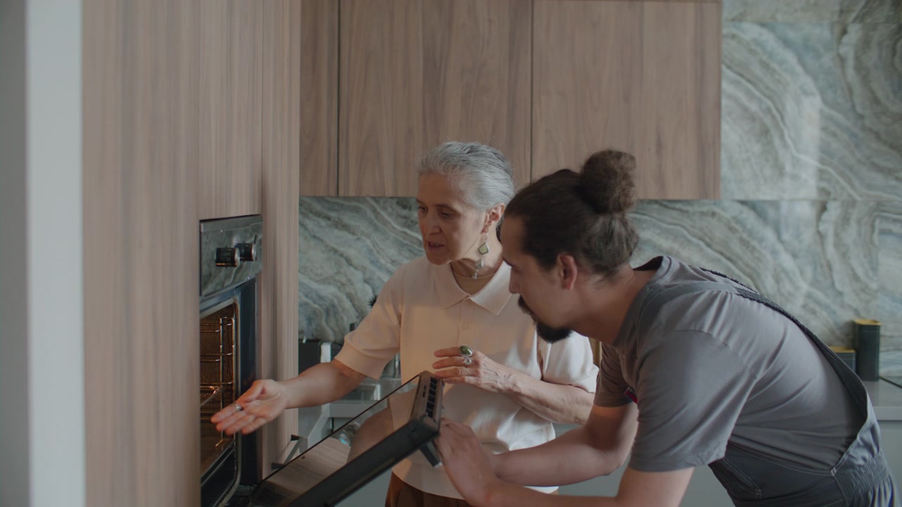 Handyman and Senior Woman Examining Built-In Kitchen Oven