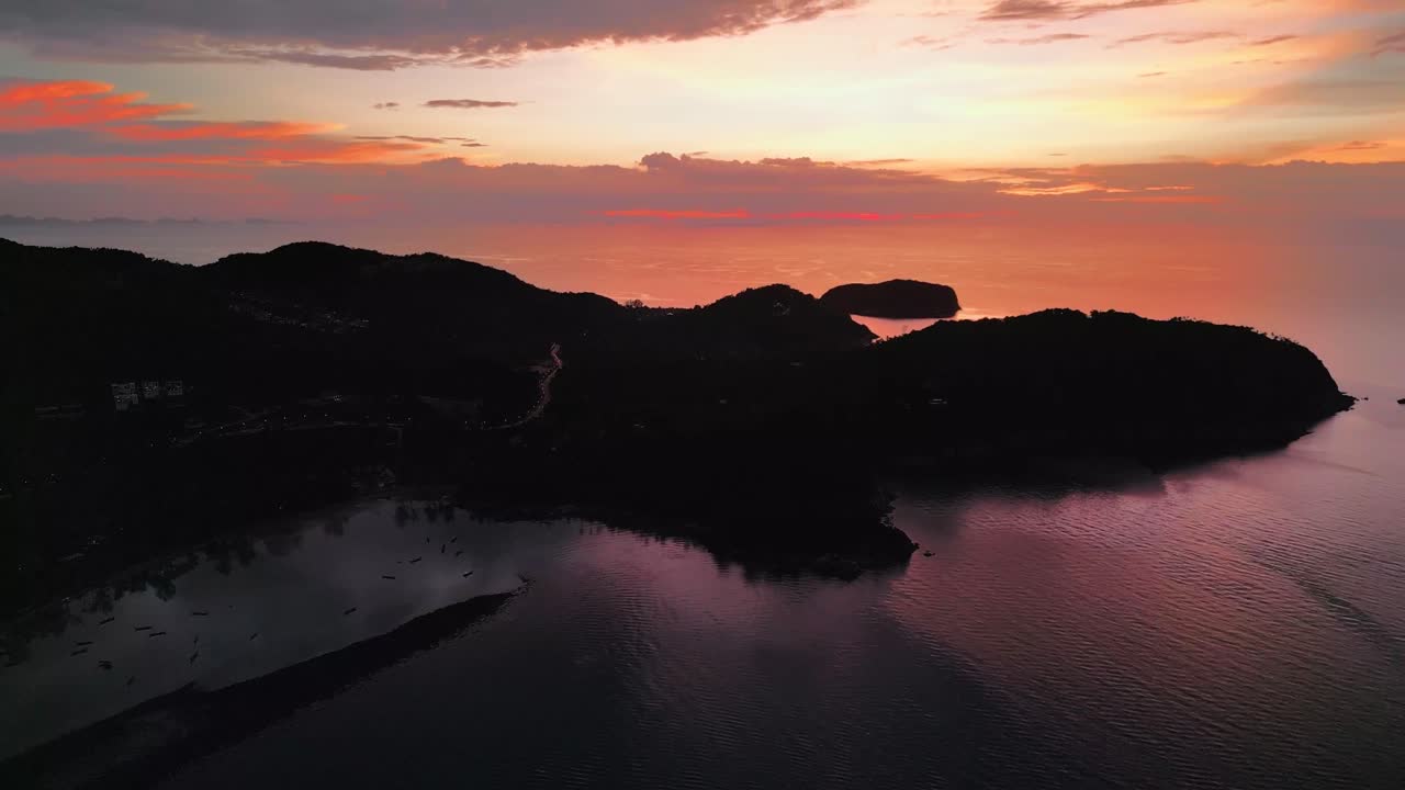 Aerial descend of Koh Phangan at golden hour, with the sun setting over calm waters and silhouetted mountains