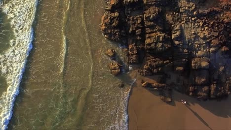 Toma-Aérea-Descendente-De-Drones-Mirando-Hacia-Abajo-En-La-Playa-Y-Las-Rocas-Con-Una-Mujer-Vagabunda