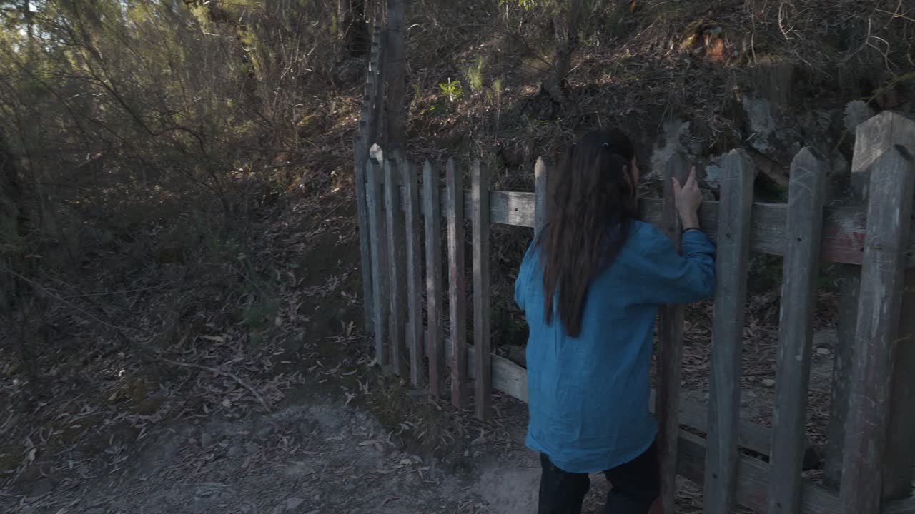 A woman stands near a rustic wooden fence on a forested hill at Warrandyte Mining Mountain, Melbourne. The serene setting offers a glimpse into the area's natural beauty