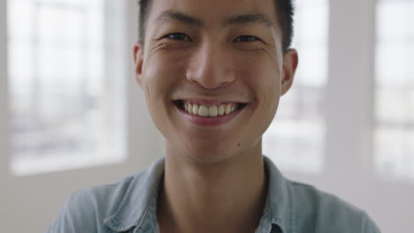 close up portrait of young asian man laughing cheerful looking at camera apartment windows background