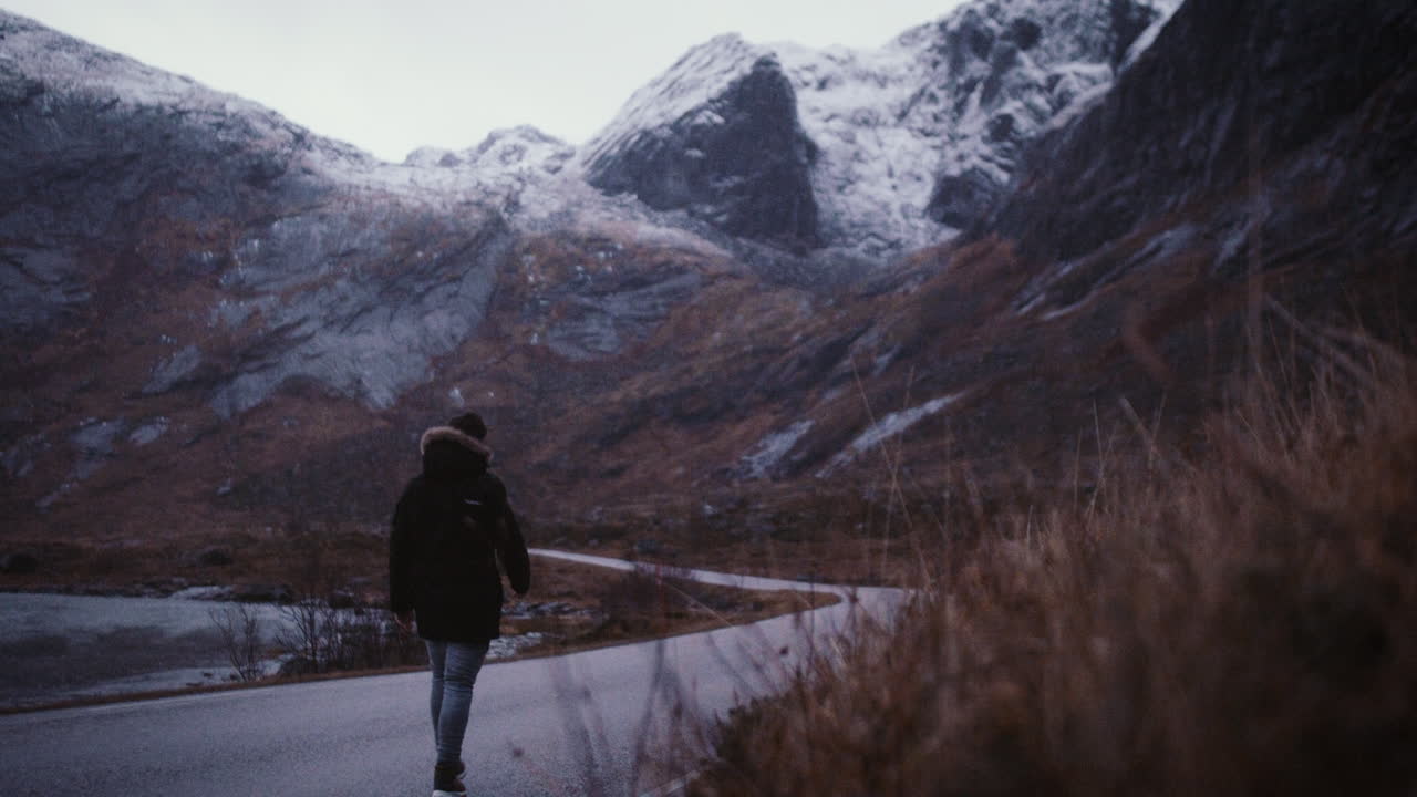 Vista posteriore di un uomo irriconoscibile che cammina su una strada di montagna, Lofoten, Norvegia